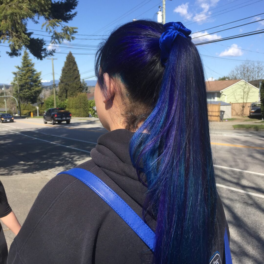 A woman with blue hair is standing on the street.