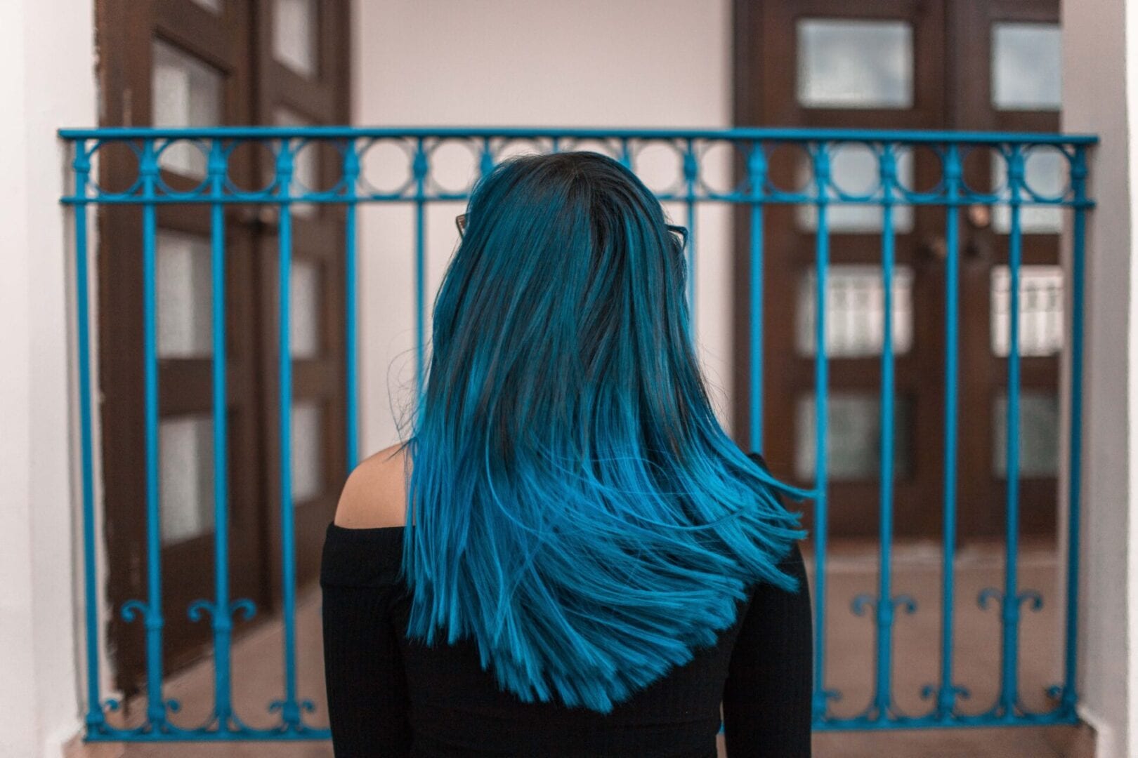 A woman with blue hair standing in front of a fence.