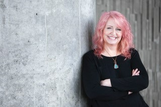 A woman with pink hair standing next to a wall.